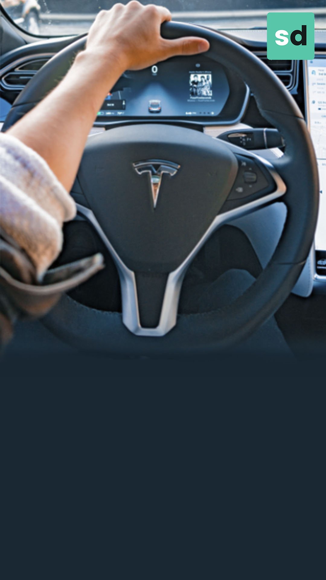 Braço de um homem caucasiano por cima do volante de um carro da montadora de veículos elétricos, Tesla 